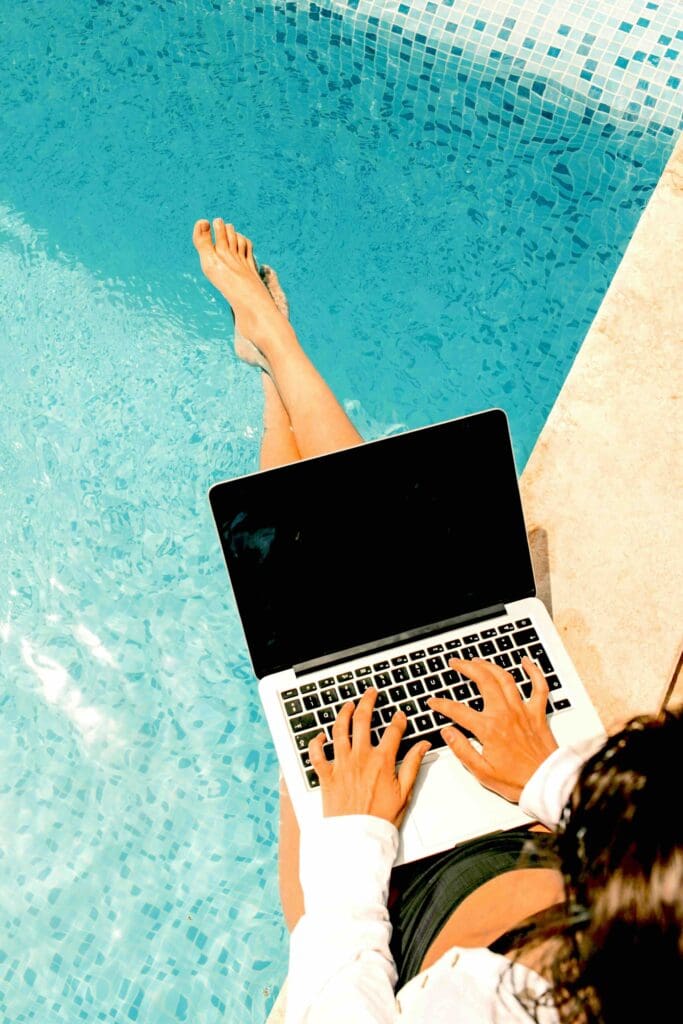 Personne travaillant sur un ordinateur portable au bord d’une piscine, illustrant la thématique du voyage en astrocartographie.
